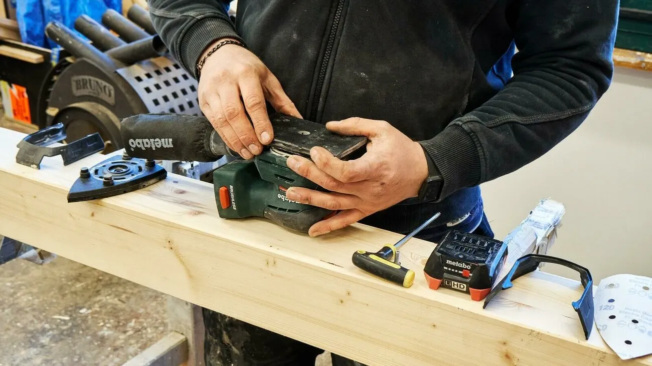 Handwerker tauscht die dreieckige Schleifplatte durch eine quadratische aus.